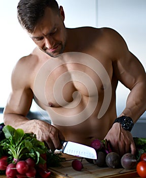 Strong sport man ready to cook cut beetroot vegetables on kitchen background healthy eating concept