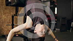 Strong sportive girl with athletic body working on her abs and core muscles using special gym set called abdominal bench
