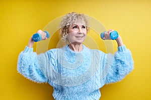 Strong Sportive Senior Woman Lifting Dumbbells Up Isolated On Yellow Background