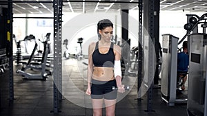 Strong sportive woman with bandaged elbow lifting dumbbell, body recovery