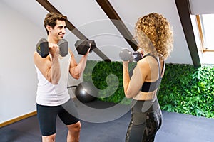 Strong sportswoman lifting dumbbells with personal trainer