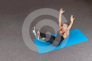 Strong and sporty fitness woman in black sportswear doing abdominal exercises and holding hands up on blue yoga mat at gym. Sport