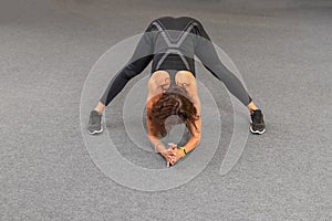 Strong and sporty fitness woman in black sportswear doing stretching exercises at gym. Copy space for text