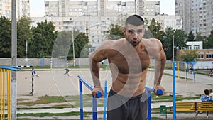 Strong sporty man doing push ups on parallel bars at sports ground. Young athlete exercising at playground. Muscular