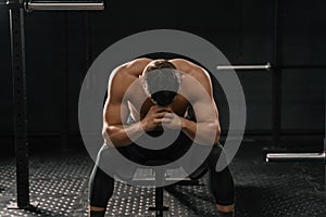 Strong sporty man sitting on gym bench suffering breakdown to overcome