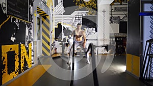 Strong sporty man training with battle ropes in sport club. Young muscular sportsman exercising at modern gym. Athletic