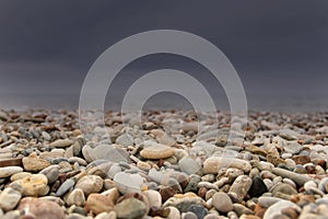 Strong storm is approaching from the sea on the shingle beach. Dark storm clouds and sunlit pebbles.