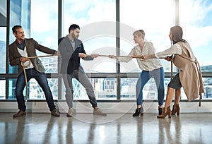 Only the strong survive in business. a group of businesspeople pulling on a rope during tug of war in an office.