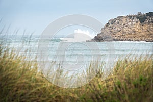 Strong wave crashing to a cliff with water splashing and green grass visible at the bottom