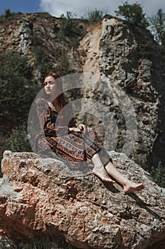 Strong-willed free strong red-haired woman in an ethnic dress near a big stone. A symbol of indomitability