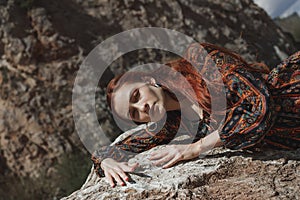 Strong-willed free strong red-haired woman in an ethnic dress near a big stone. A symbol of indomitability