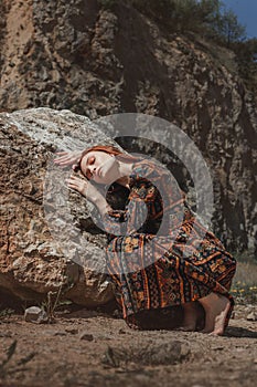 Strong-willed free strong red-haired woman in an ethnic dress near a big stone. A symbol of indomitability