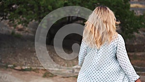 Strong-willed girl with light flowing blond hair strides forward to meet fate, lady in white polka-dot blouse, flying in