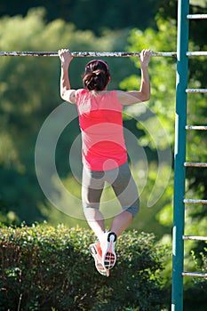 Strong woman athlete is Chin-ups and Pullups training on an abandoned sports field. Pull-up on the bar. Athlete Outdoors.