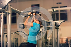 Strong woman in blue t-shirt and black pants exercising in a gym - doing pull-ups.