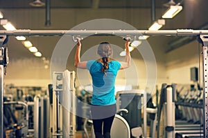 Strong woman in blue t-shirt and black pants exercising in a gym - doing pull-ups..