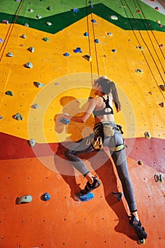 Strong woman climbing up the orange wall in gym