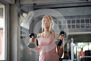 Strong woman doing exercises with dumbbells in gym
