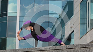 Strong woman in hijab flexible girl doing yoga exercises on street city building background sport lady stands in side