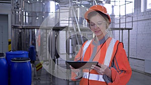 Strong woman at manufactory, factory worker female into helmet and overall with digital tablet making calculated