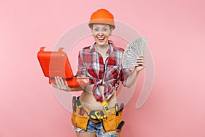 Strong woman in orange helmet, plaid shirt, denim shorts, kit tools belt full of instruments, toolbox, lots cash money