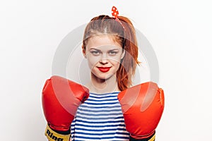 Strong woman in red boxing gloves and in a striped t-shirt front view light background