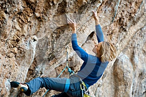 strong woman rock climber climbing difficult route on cliff, making hard move up