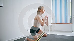 Strong woman squats workout home. Athletic girl fitness using stretching strap