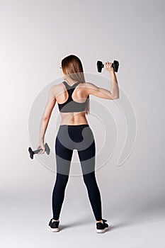 Strong woman working out with dumbbells, flexing her arm. Photo of sporty woman in sportswear on white background. Rear