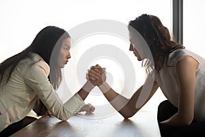 Strong women arm wrestle at work struggle for leadership