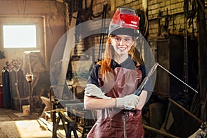 Strong and worthy pretty redhead ginher woman wearing protection helmet and leather apron with gloves holding welding