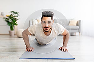 Strong young Arab man making strength workout, standing in plank pose at home