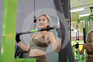 Strong young Asian woman exercising with pulldown machine in a fitness club, doing exercises in gym