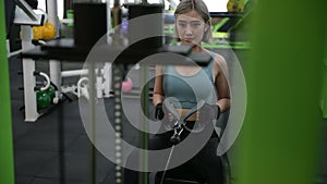 Strong young Asian woman exercising with pulldown machine in a fitness club, doing exercises in gym