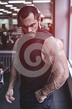 Strong young bearded caucasian male athlete with big muscles wearing black sportswear in sport fitness gym