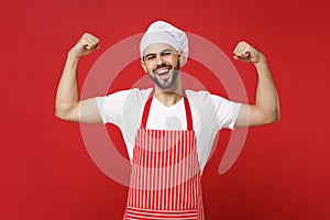 Strong young bearded male chef cook or baker man in striped apron white t-shirt toque chefs hat posing isolated on red