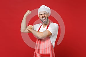 Strong young bearded male chef cook or baker man in striped apron white t-shirt toque chefs hat posing isolated on red