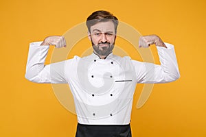 Strong young bearded male chef cook or baker man in white uniform shirt posing isolated on yellow wall background studio