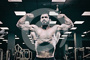 strong young bearded male showing double biceps muscle in dark sport gym during training