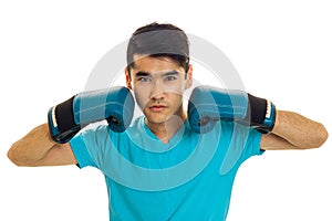 Strong young brunette man in blue gloves practicing boxing and looking at the camera isolated on white background