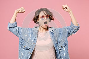 Strong young brunette woman girl in casual denim jacket, eyeglasses posing isolated on pastel pink background studio