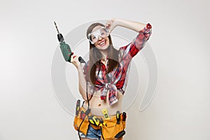 Strong young energy handyman woman in plaid top shirt denim shorts kit tools belt full of instruments in protective
