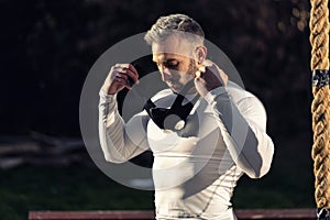 Strong young good looking man with fitness mask standing next to a hanging rope outside in the neighborhood, street workout