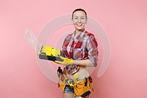 Strong young handyman woman in plaid shirt, denim shorts, kit tools belt full of different instruments holding toolbox