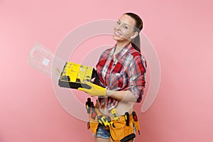 Strong young handyman woman in plaid shirt, denim shorts, kit tools belt full of different instruments holding toolbox