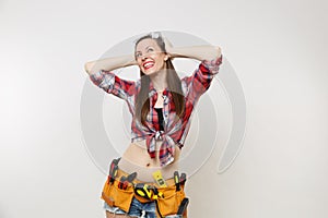 Strong young handyman woman in plaid top shirt, denim shorts, kit tools belt full of instruments in protective goggles