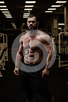 strong young male with beard and perfect fitness abdominal muscles in sport gym in night