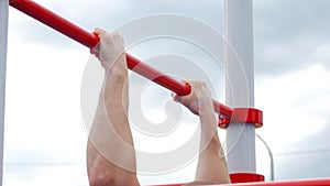 Strong young man making pull ups exercises. Close up of strong athlete doing pull-up on horizontal bar outdoors. Sport