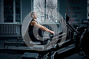 Strong young man in a t-shirt and shorts doing exercises on the simulators in the gym looking to the side