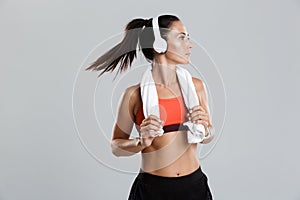 Strong young sports woman isolated indoors with towel on neck listening music with headphones.